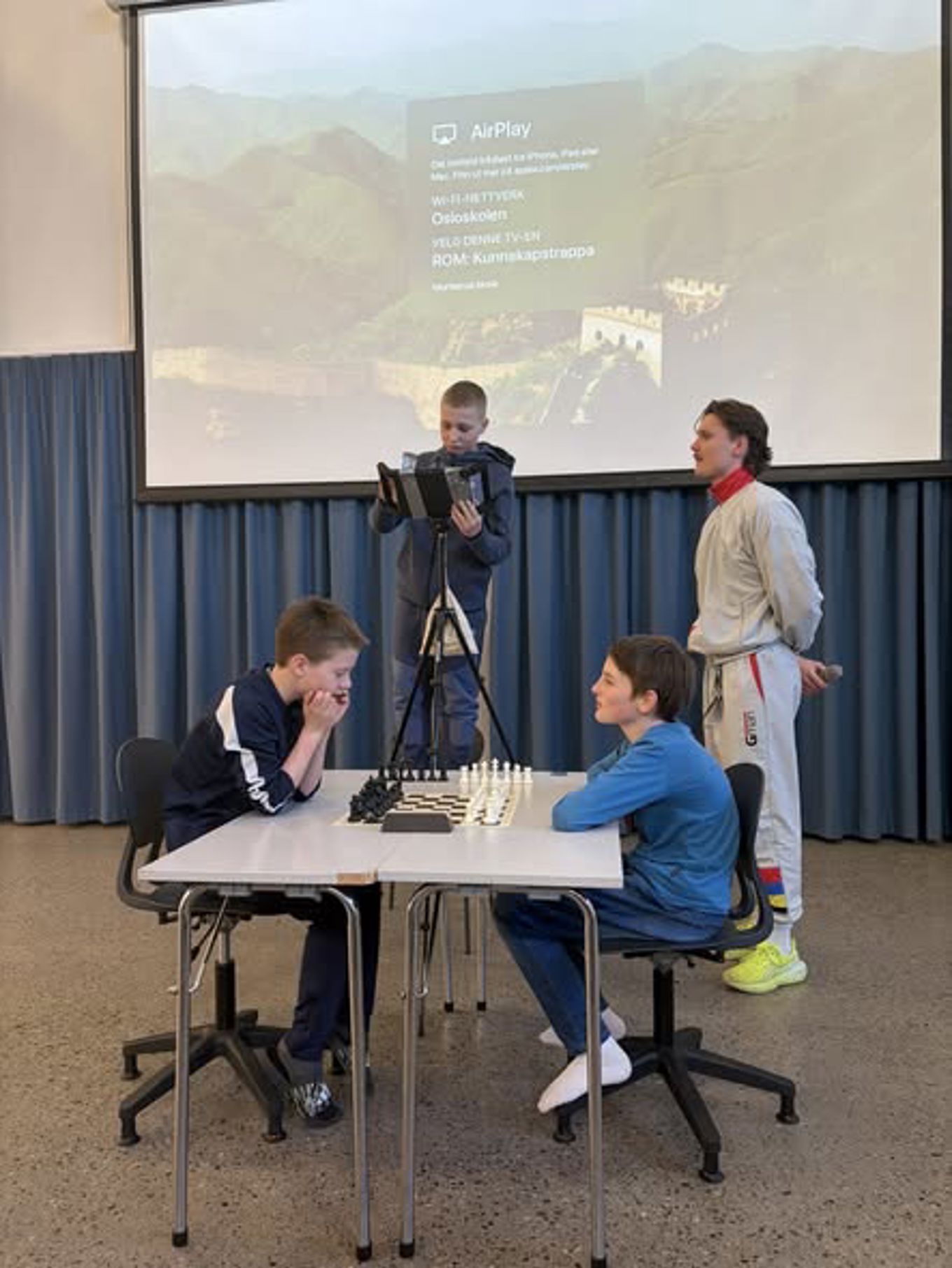 En gruppe mennesker som sitter ved et bord med en projektorskjerm bak seg